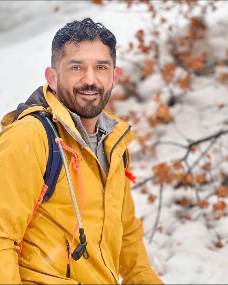 Roy Benites smiling in a yellow jacket on a snowy mountain trail